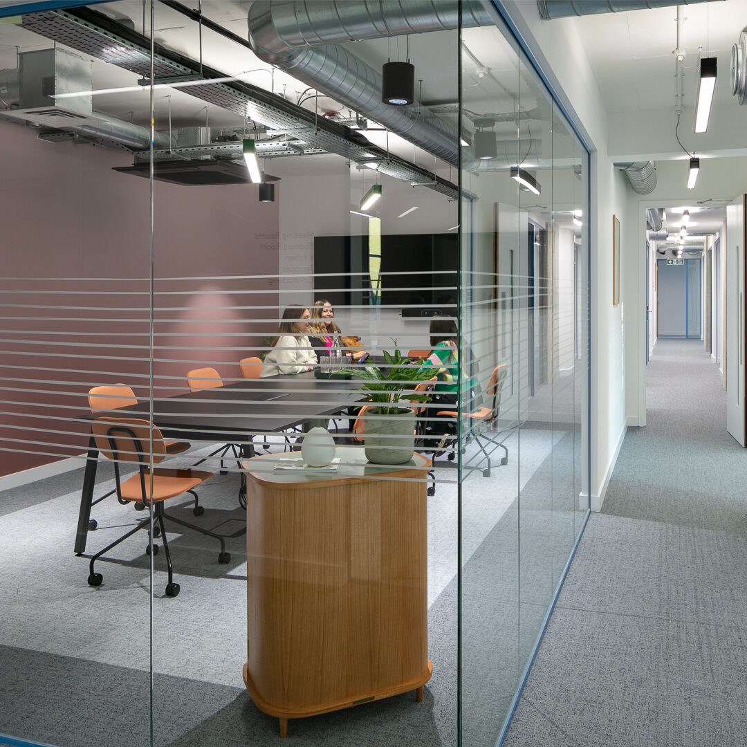 Glass-fronted meeting room within an enterprise suite in a coworking space in Putney, featuring modern furnishings, warm-toned chairs, and a collaborative workspace environment.