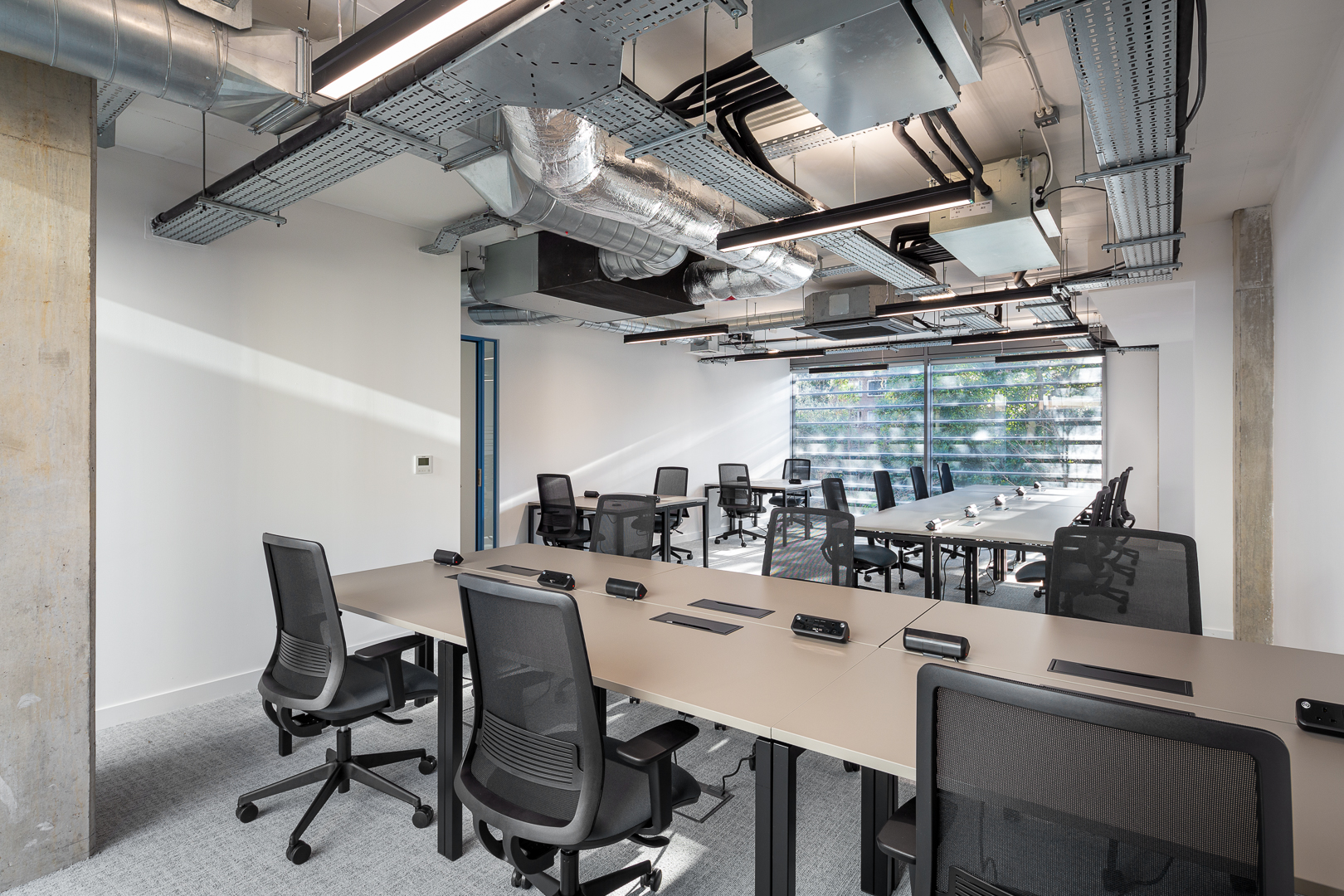 Spacious private office for large teams in a coworking space in Putney, featuring multiple desks, ergonomic chairs, and industrial-style design with plenty of natural light.