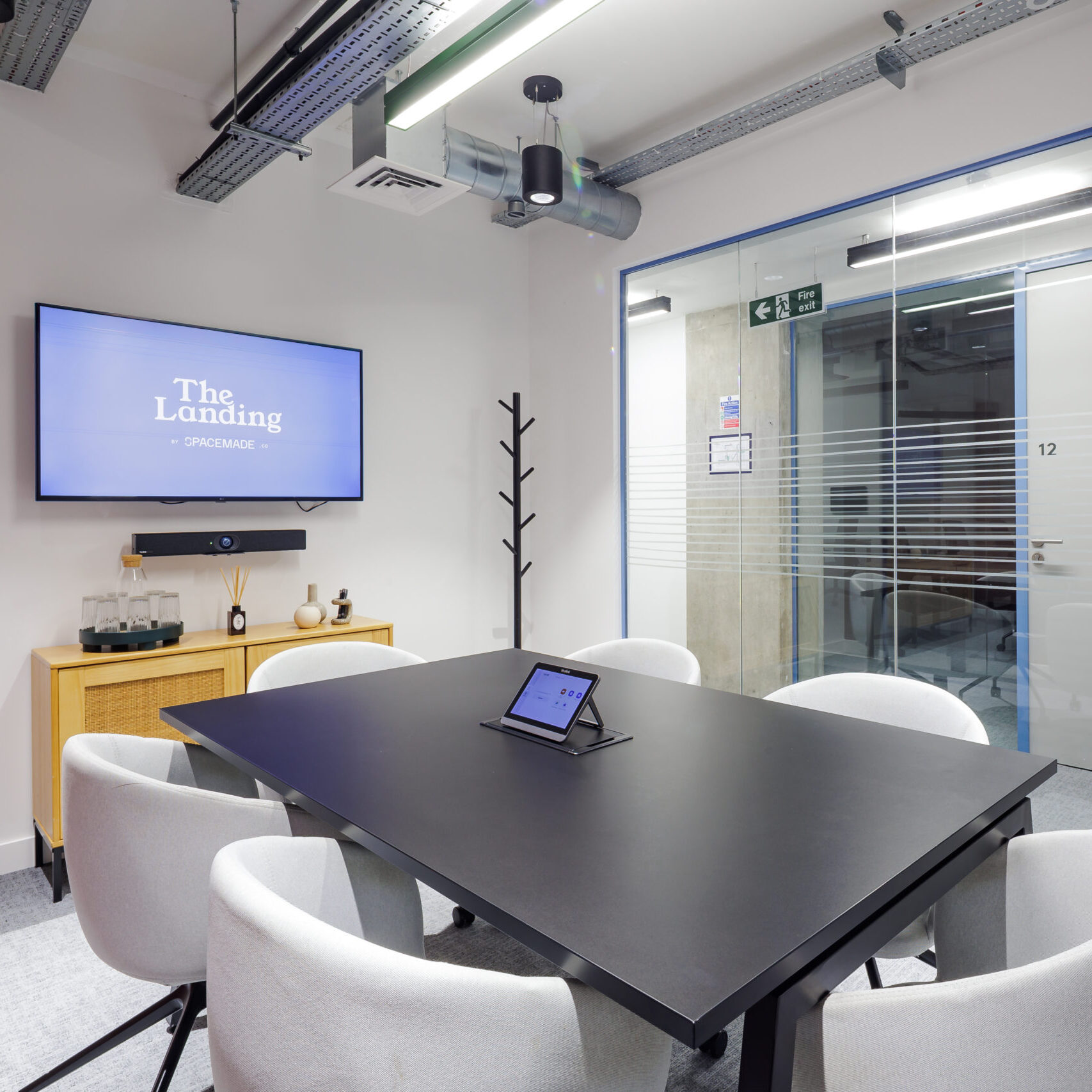 Six-person meeting room in a coworking space in Putney, featuring a sleek black table, soft upholstered chairs, video conferencing setup, and modern minimalist design.