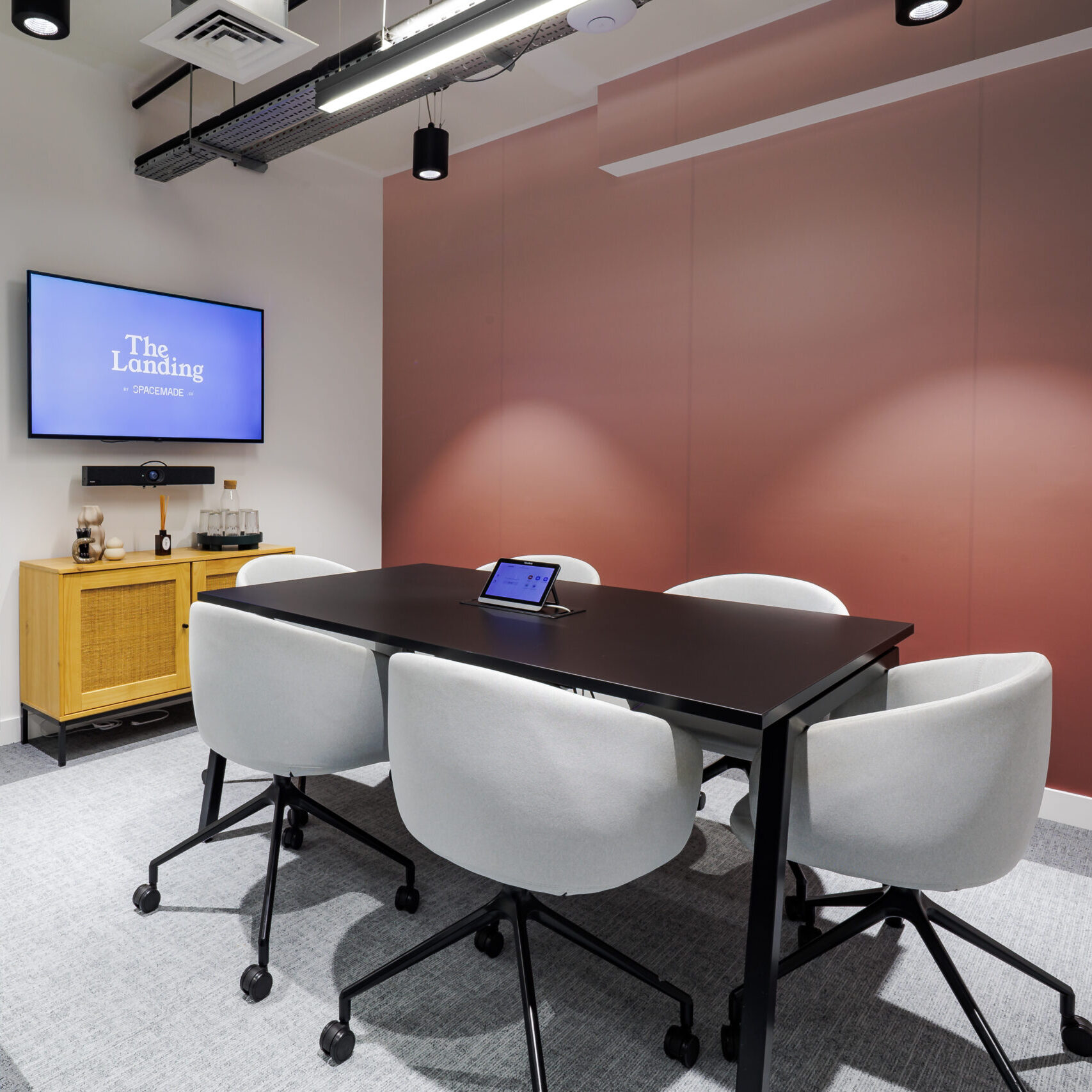 Modern meeting room within a coworking space in Putney, featuring a sleek black table, comfortable chairs, video conferencing setup, and warm, contemporary design.