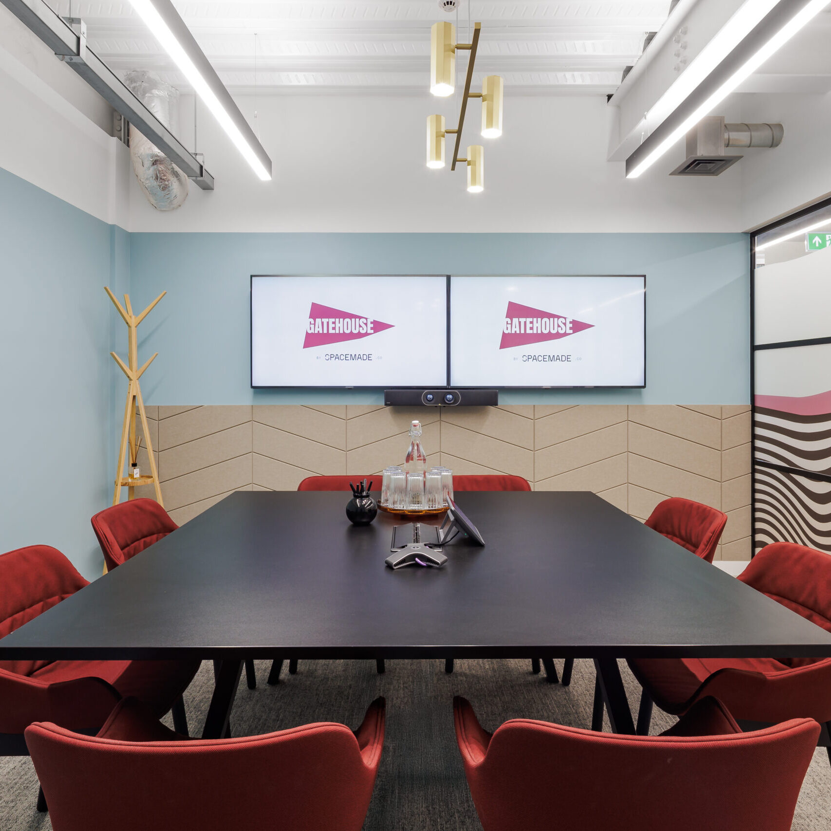 Contemporary meeting room in an office space in Wandsworth, London, featuring red chairs, dual screens for video conferencing, and modern design elements with pastel tones and graphic glass partitions.