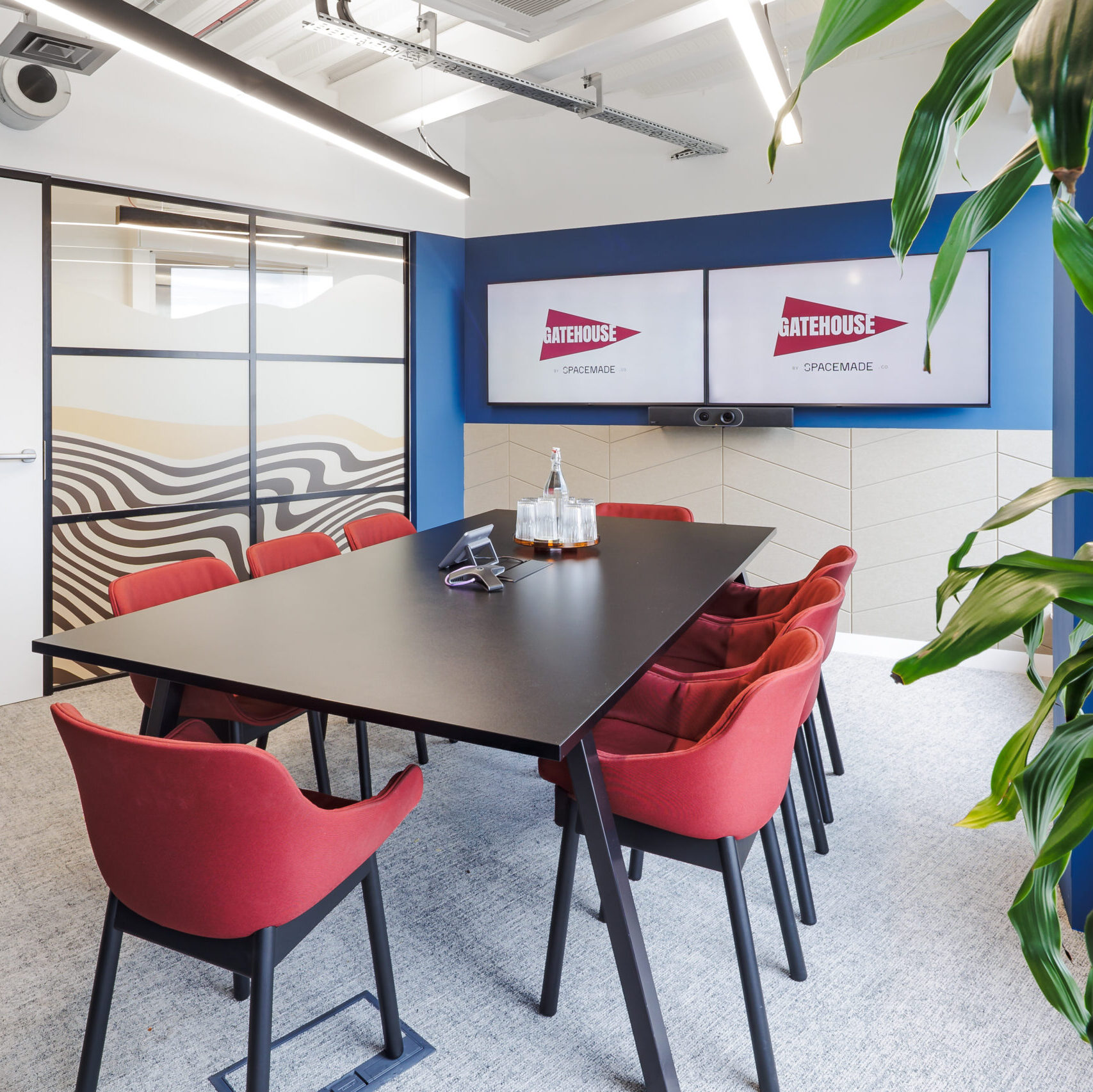 Bright and modern meeting room at a coworking space in Wandsworth, London, featuring bold red chairs, dual presentation screens, and contemporary glass wall design.