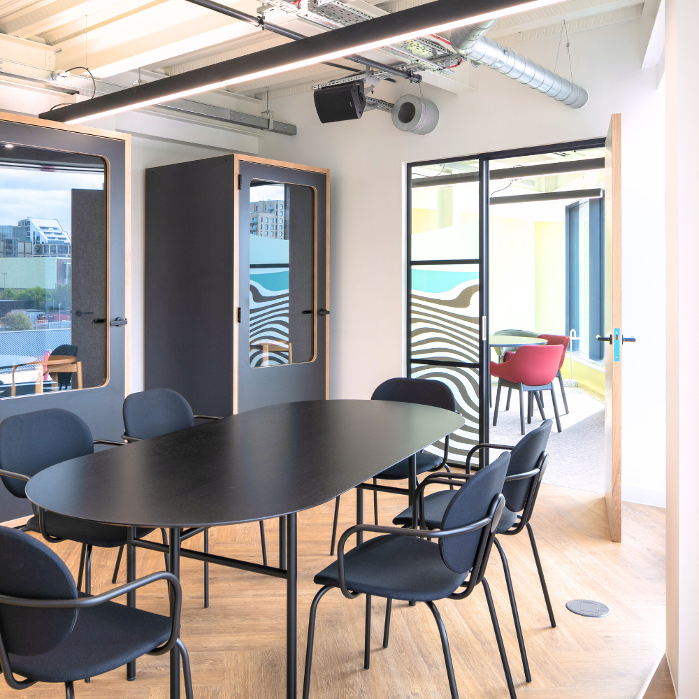 Stylish private meeting room in a serviced enterprise office, featuring a modern black table, comfortable seating, acoustic phone booths, and natural light with contemporary design elements.