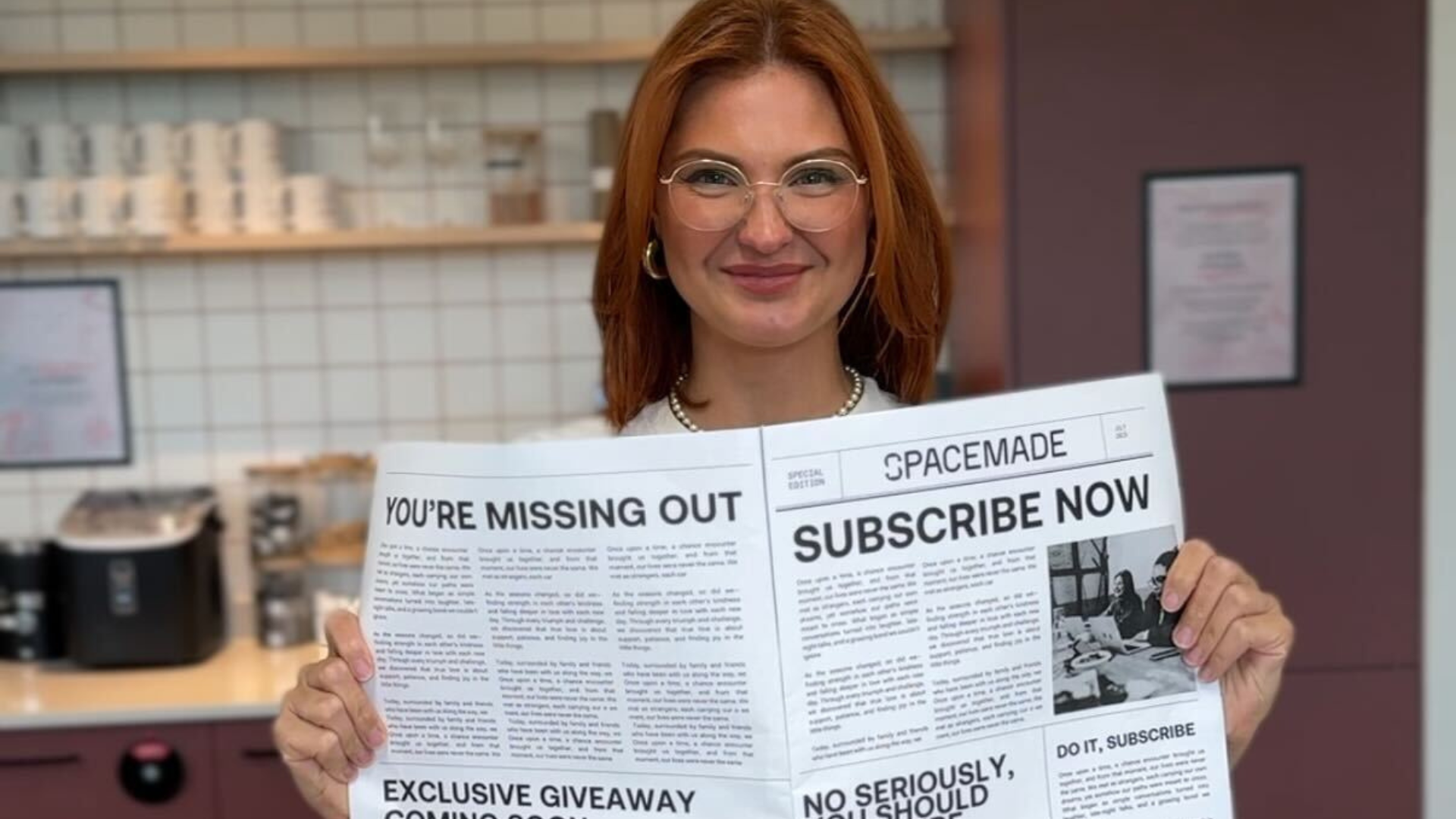 A woman with glasses smiling into the camera, holding a newspaper in her hands that reads "Subscribe now"