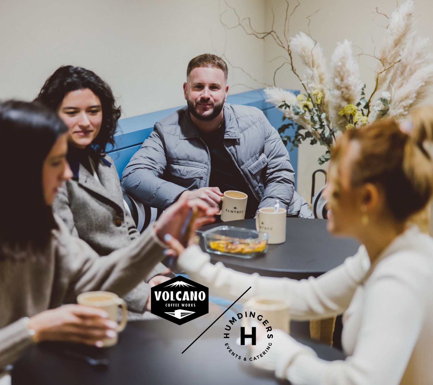 A group of people chatting over a cup of coffee with two logos at the bottom of the image: "Volcano coffee" and "Humdingers catering"