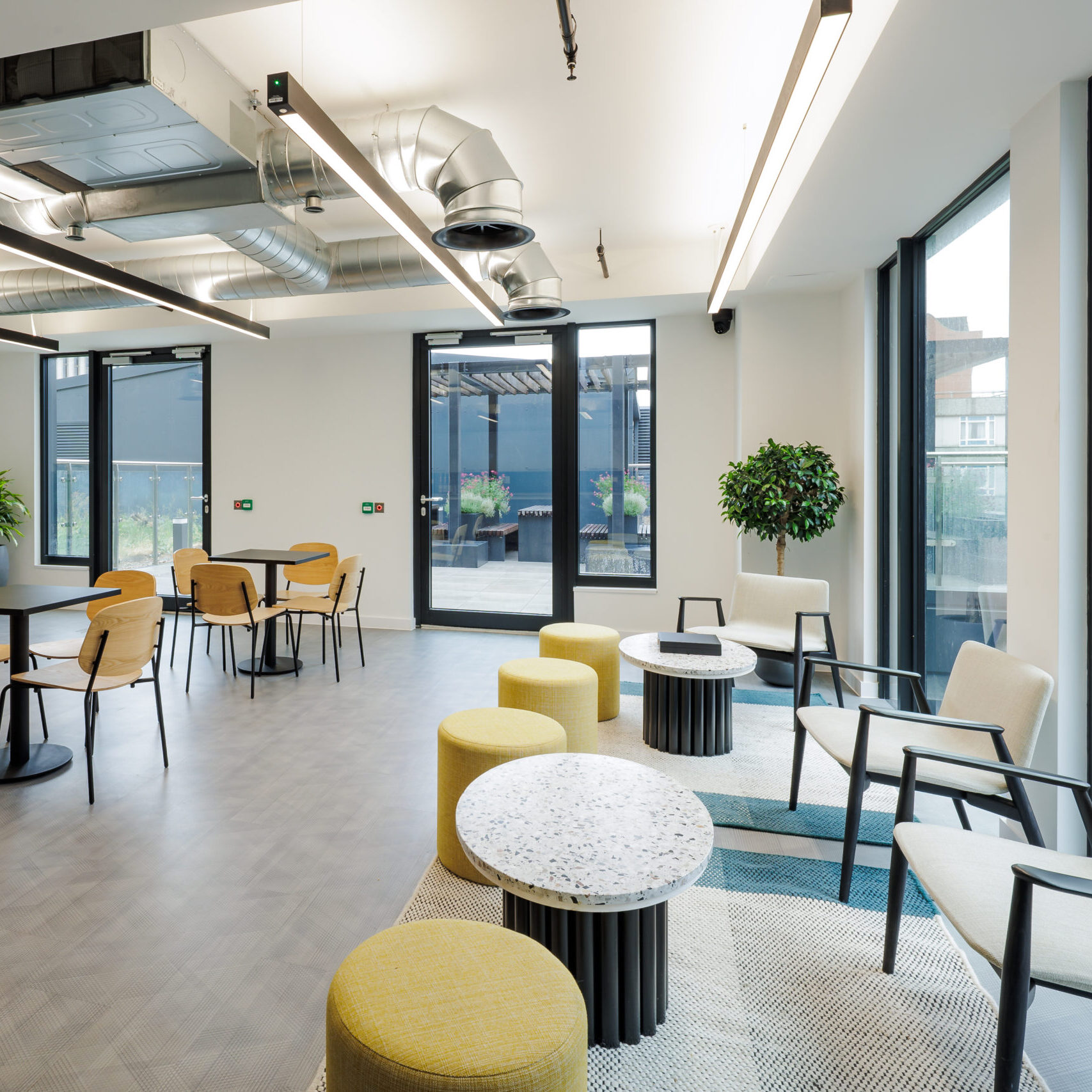 Rooftop & clubhouse at 10X is event venue in Birmingham, featuring contemporary lounge seating, café-style tables, floor-to-ceiling windows, and access to a landscaped outdoor terrace.