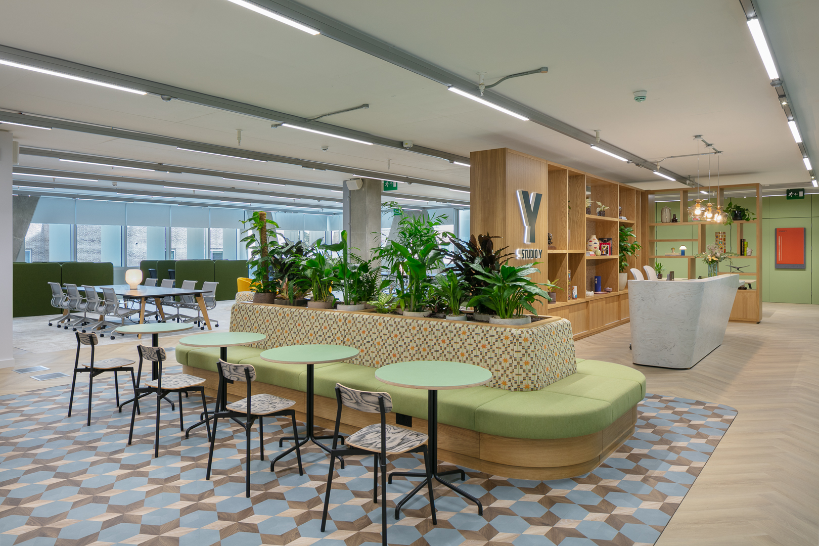 Modern and vibrant reception area at Studio Y coworking space in Notting Hill, featuring lush indoor plants, a patterned bench, geometric flooring, and a sleek white marble desk set against warm wooden shelving. Modern and vibrant reception area at Studio Y coworking space in Notting Hill, featuring lush indoor plants, a patterned bench, geometric flooring, and a sleek white marble desk set against warm wooden shelving.