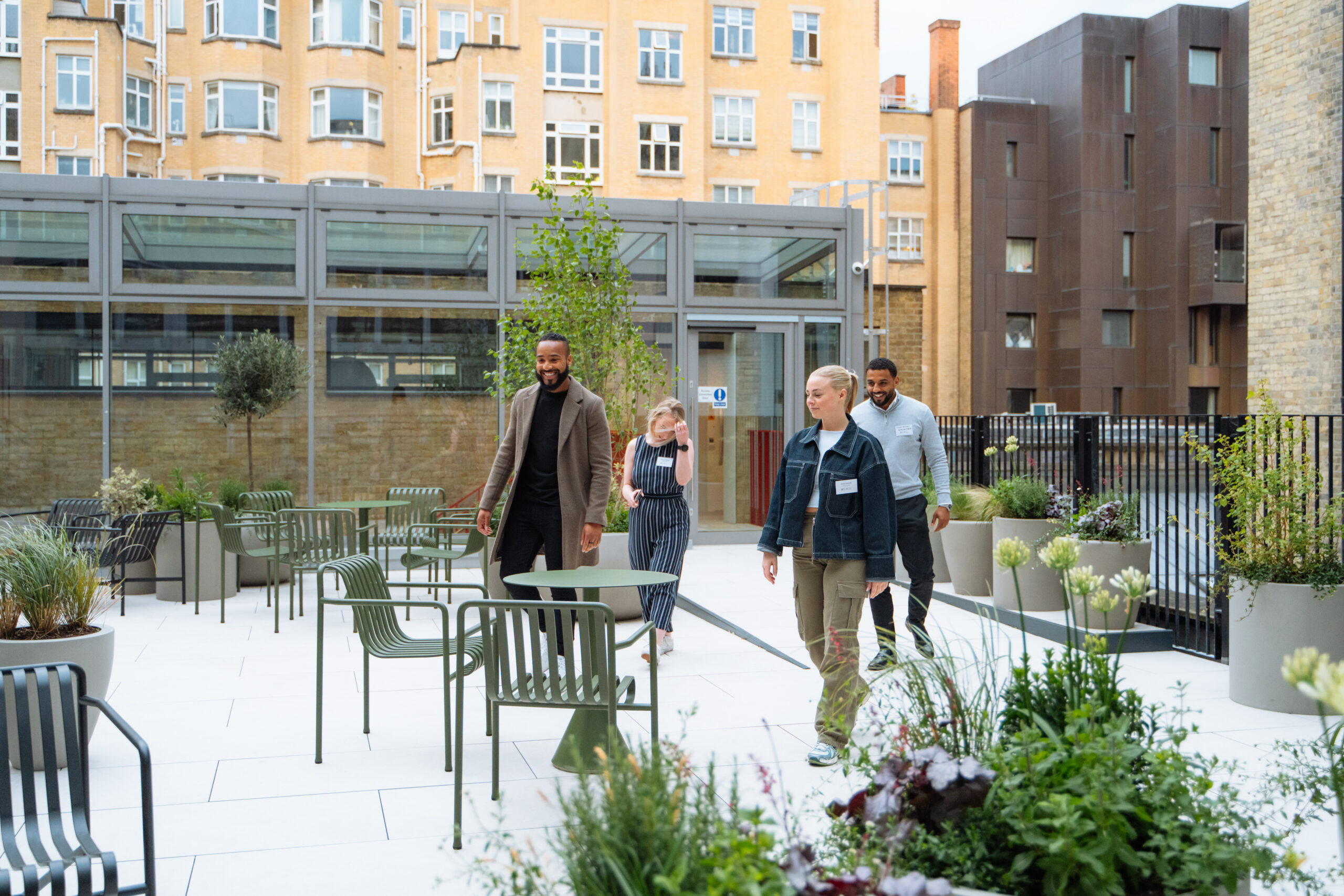 Group of professionals walking through a modern rooftop terrace at a healthtech hub coworking space in London, surrounded by greenery and urban buildings.