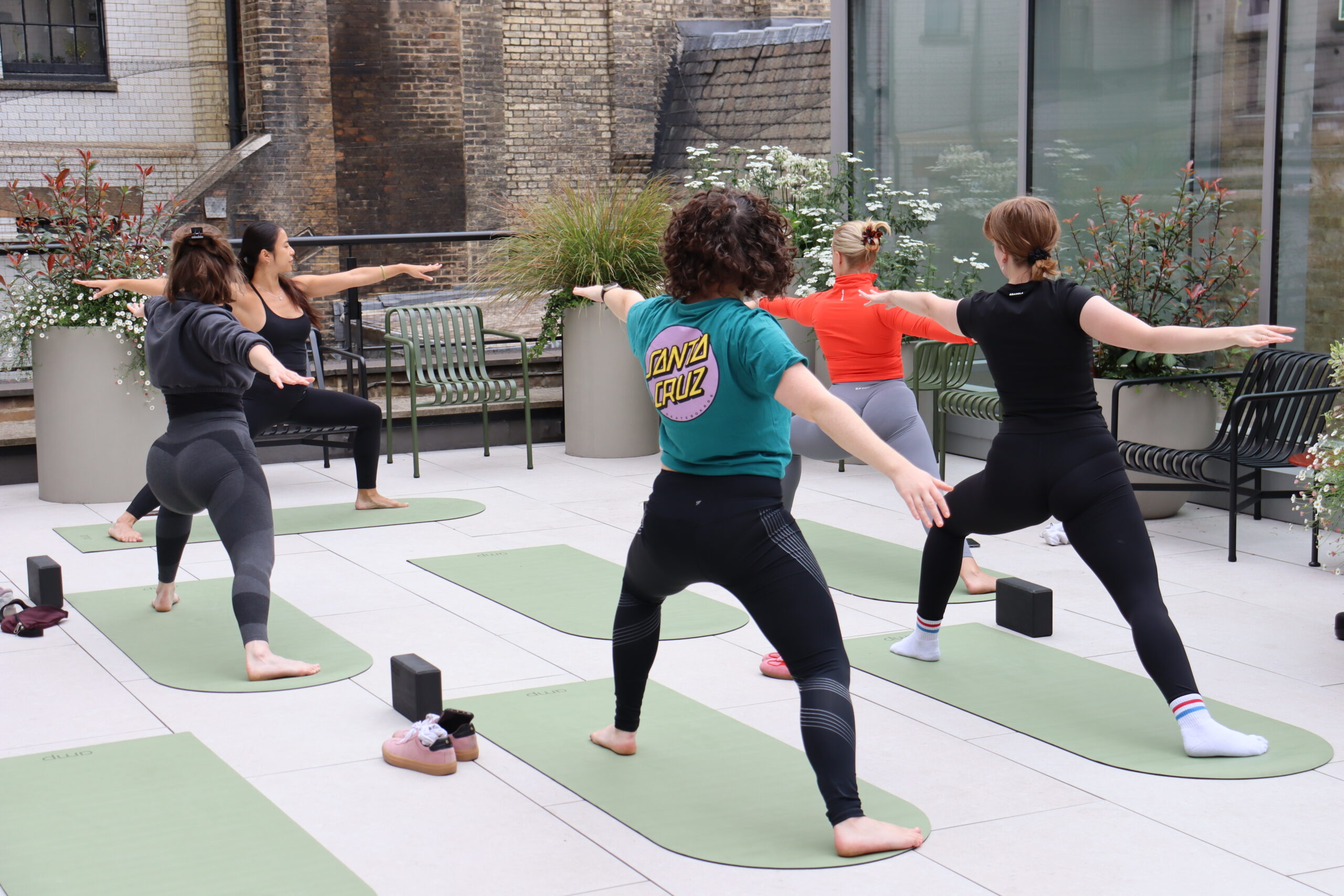 Group of people practising yoga outdoors on a rooftop terrace at a healthtech hub in London, surrounded by greenery and urban architecture. Group of people practising yoga outdoors on a rooftop terrace at a healthtech hub in London, surrounded by greenery and urban architecture.