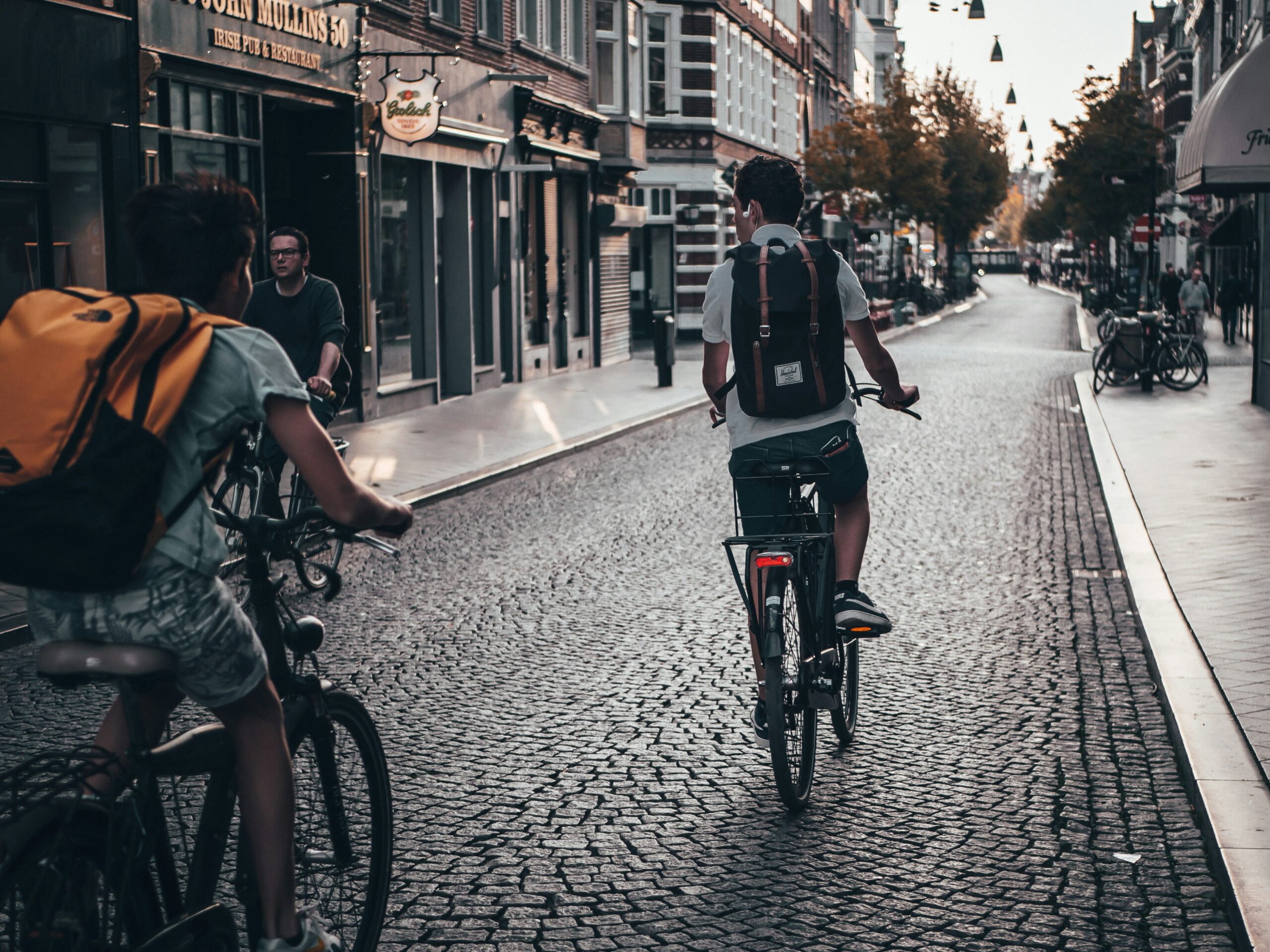 People cycling to work down a quiet, cobblestone street lined with shops and cafes in an urban city. People cycling to work down a quiet, cobblestone street lined with shops and cafes in an urban city.